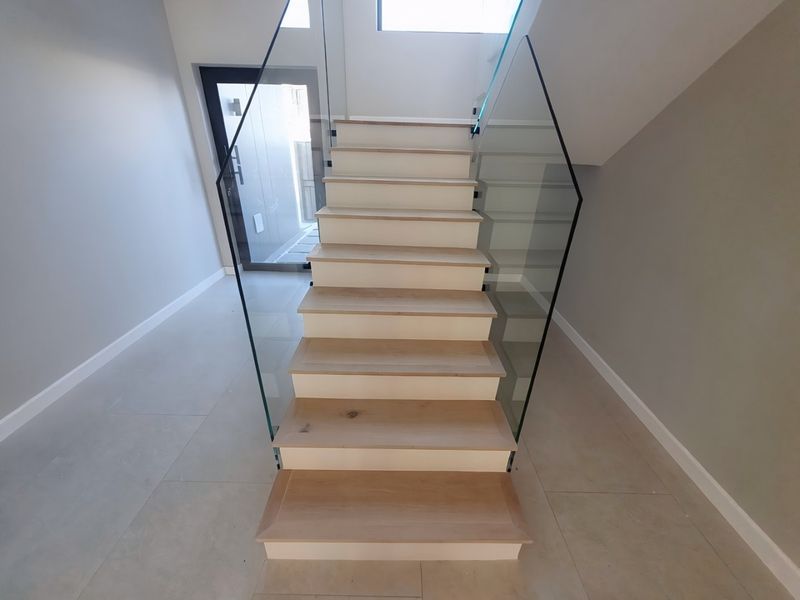 Modern entrance foyer featuring a timber staircase with a sleek glass balustrade and neutral tiled flooring.