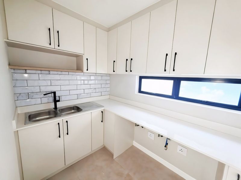 A modern, clean scullery featuring white cabinetry, quartz countertops, a stainless steel double sink, and a stylish subway tile backsplash.