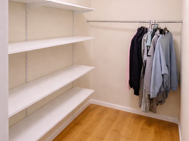 A walk-in closet or storage area featuring white built-in shelving, a metal hanging rail, and wood-look laminate flooring.