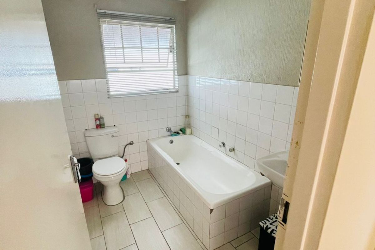 A functional bathroom featuring a bathtub, toilet, and washbasin with tiled finishes, currently showing signs of ceiling water damage and wear.