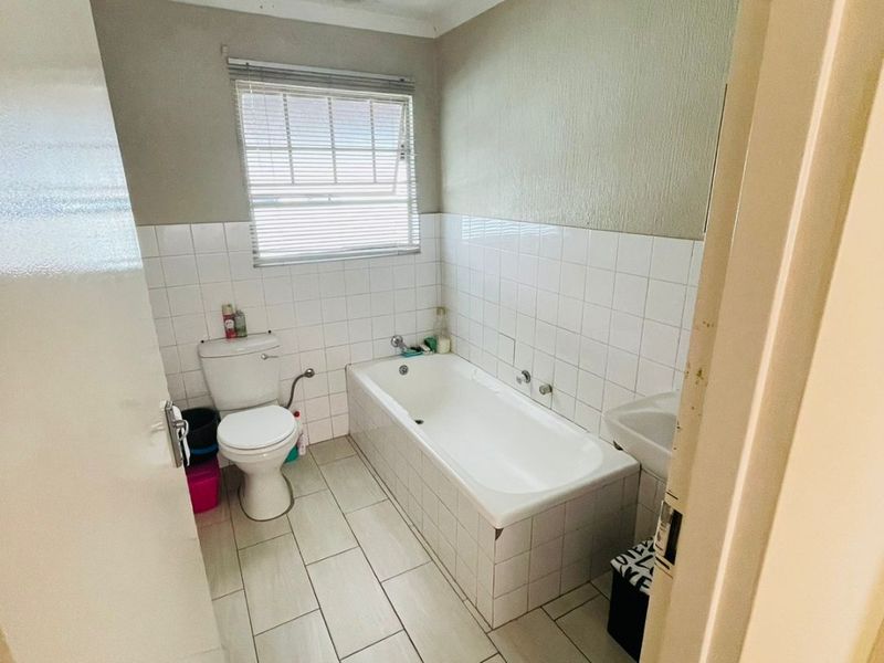 A functional bathroom featuring a bathtub, toilet, and washbasin with tiled finishes, currently showing signs of ceiling water damage and wear.