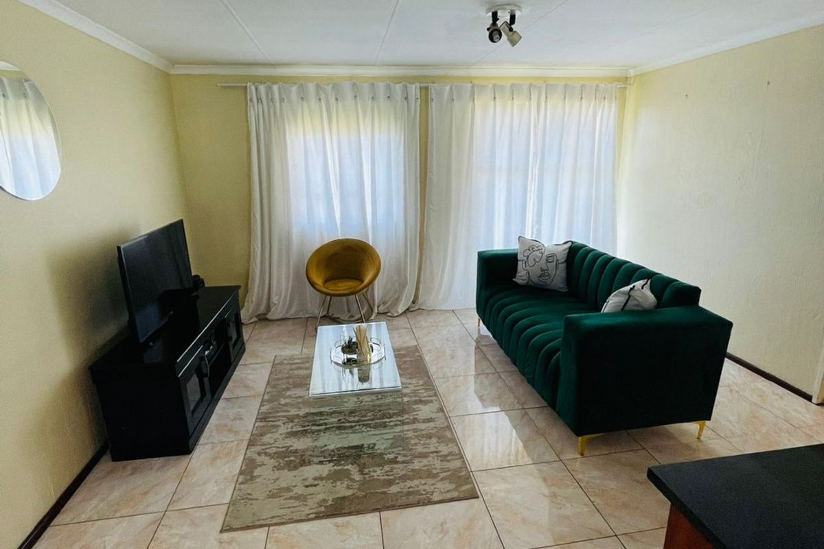A living room area featuring tiled flooring, neutral wall finishes, and large windows with curtain tracks, providing a functional and well-lit space.