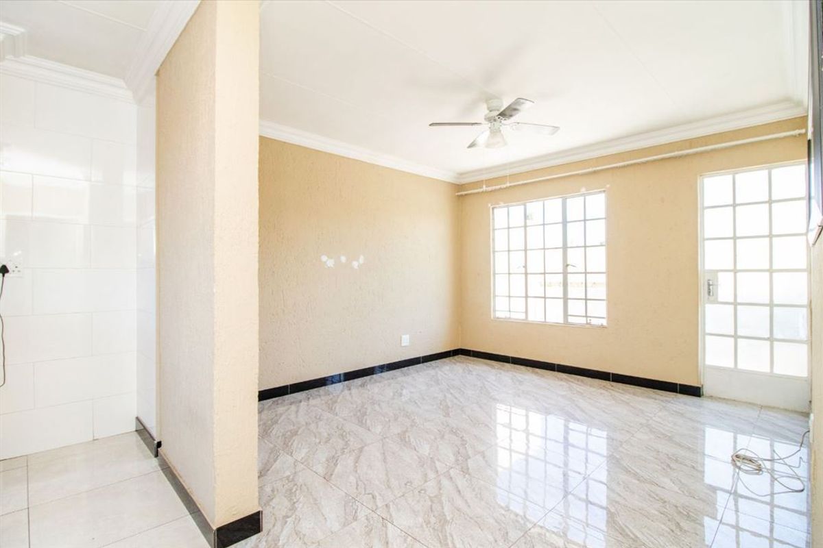 A bright, empty living area featuring modern marble-look tiled flooring, a ceiling fan, and natural light through grid-style windows and a glass panel door.