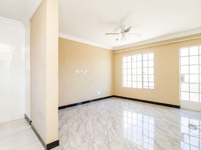 A bright, empty living area featuring modern marble-look tiled flooring, a ceiling fan, and natural light through grid-style windows and a glass panel door.