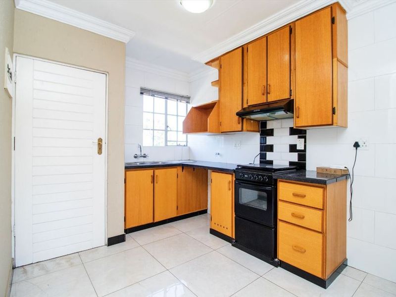 A functional kitchen featuring wooden cabinetry, laminate countertops, a built-in oven with extractor fan, and tiled flooring throughout.