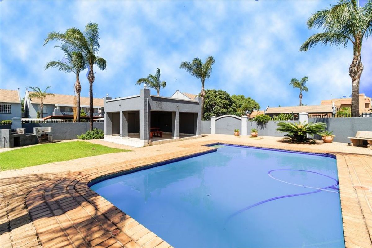 Outdoor entertainment area featuring a swimming pool, covered patio structure, and built-in braai, set within a walled garden with established palm trees.