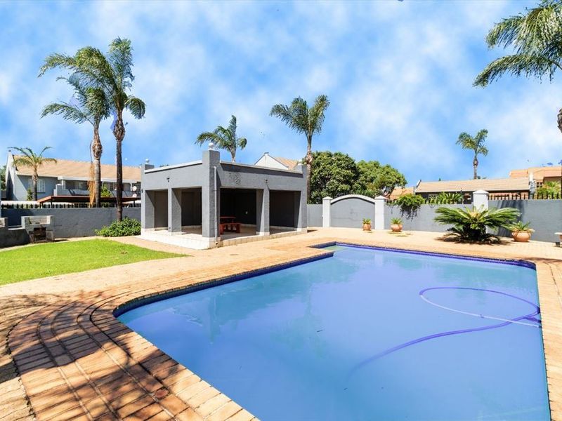 Outdoor entertainment area featuring a swimming pool, covered patio structure, and built-in braai, set within a walled garden with established palm trees.