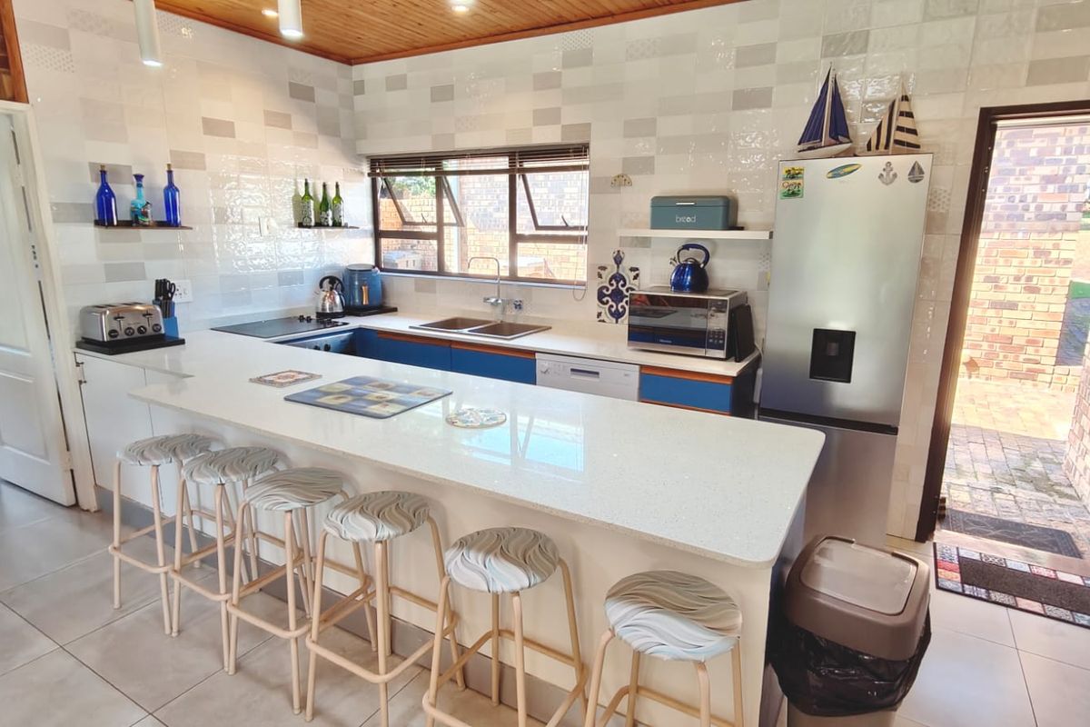 A functional kitchen featuring a large quartz breakfast bar, double basin sink, built-in hob, and tiled splashback with a warm timber ceiling finish.