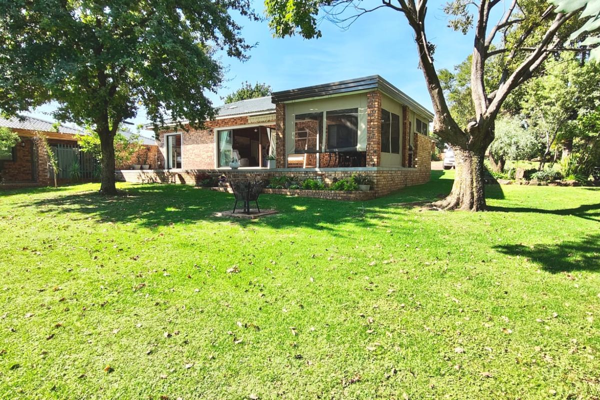 A view of the rear brick facade featuring an enclosed patio area, large sliding glass doors, and a spacious, well-maintained garden with mature trees.