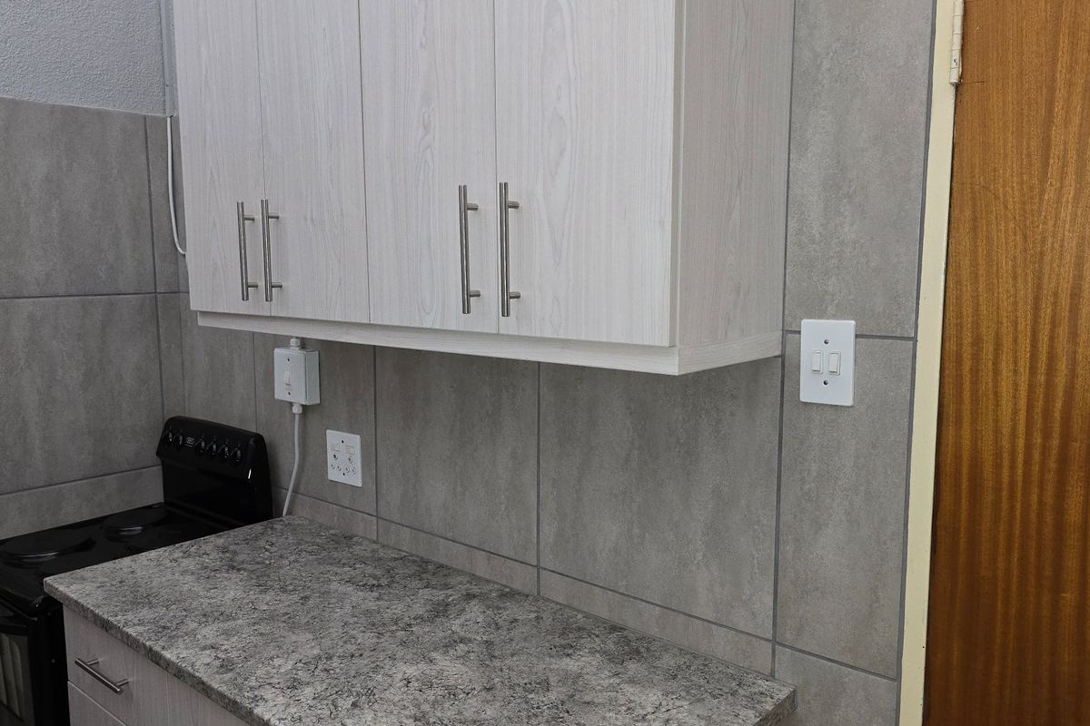 A functional kitchen area featuring light wood-grain cabinetry, stone-look countertops, grey wall tiling, and a built-in stove.