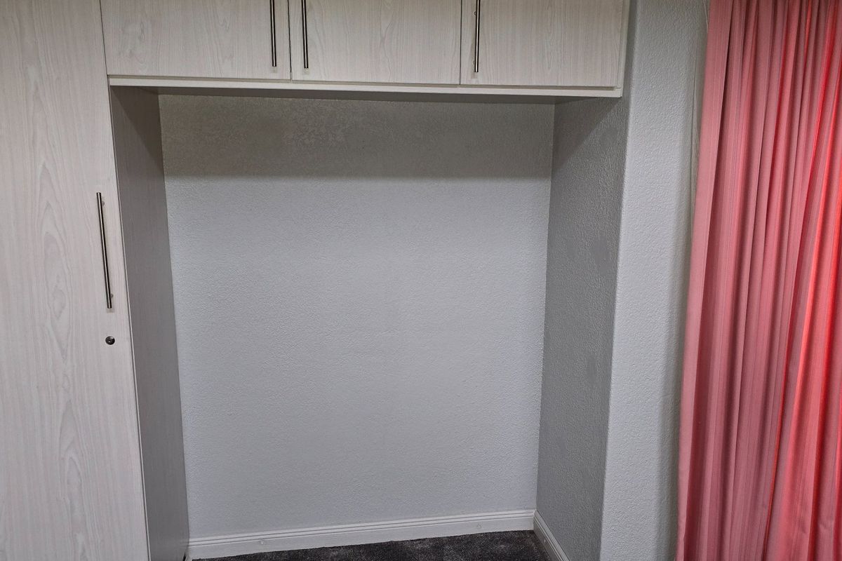 A bedroom alcove featuring built-in light wood-grain cabinetry with overhead storage cupboards.