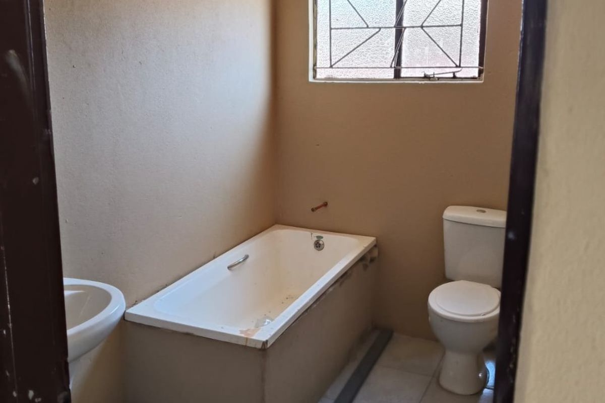A functional bathroom featuring a pedestal basin, built-in bathtub, and toilet, with tiled flooring and security bars on the window.