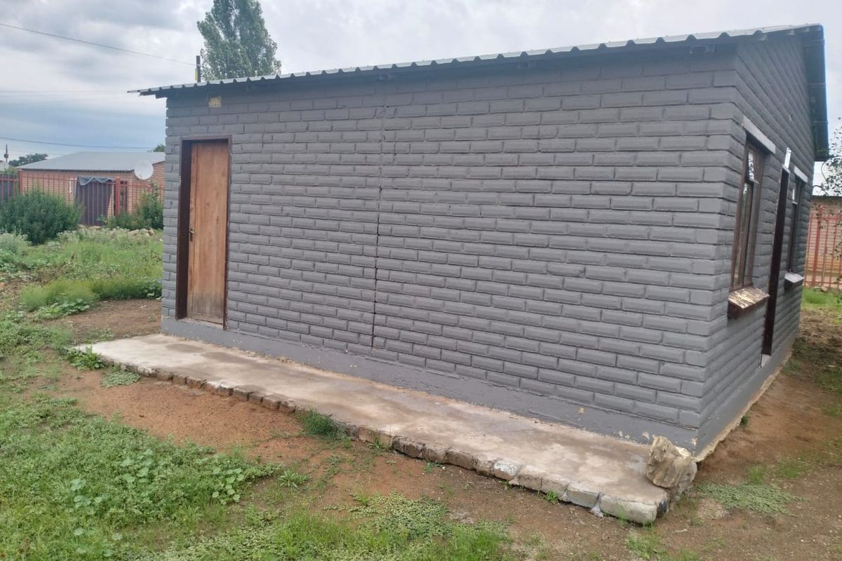 Exterior view of a detached outbuilding featuring painted brick walls, a corrugated metal roof, and a concrete apron.