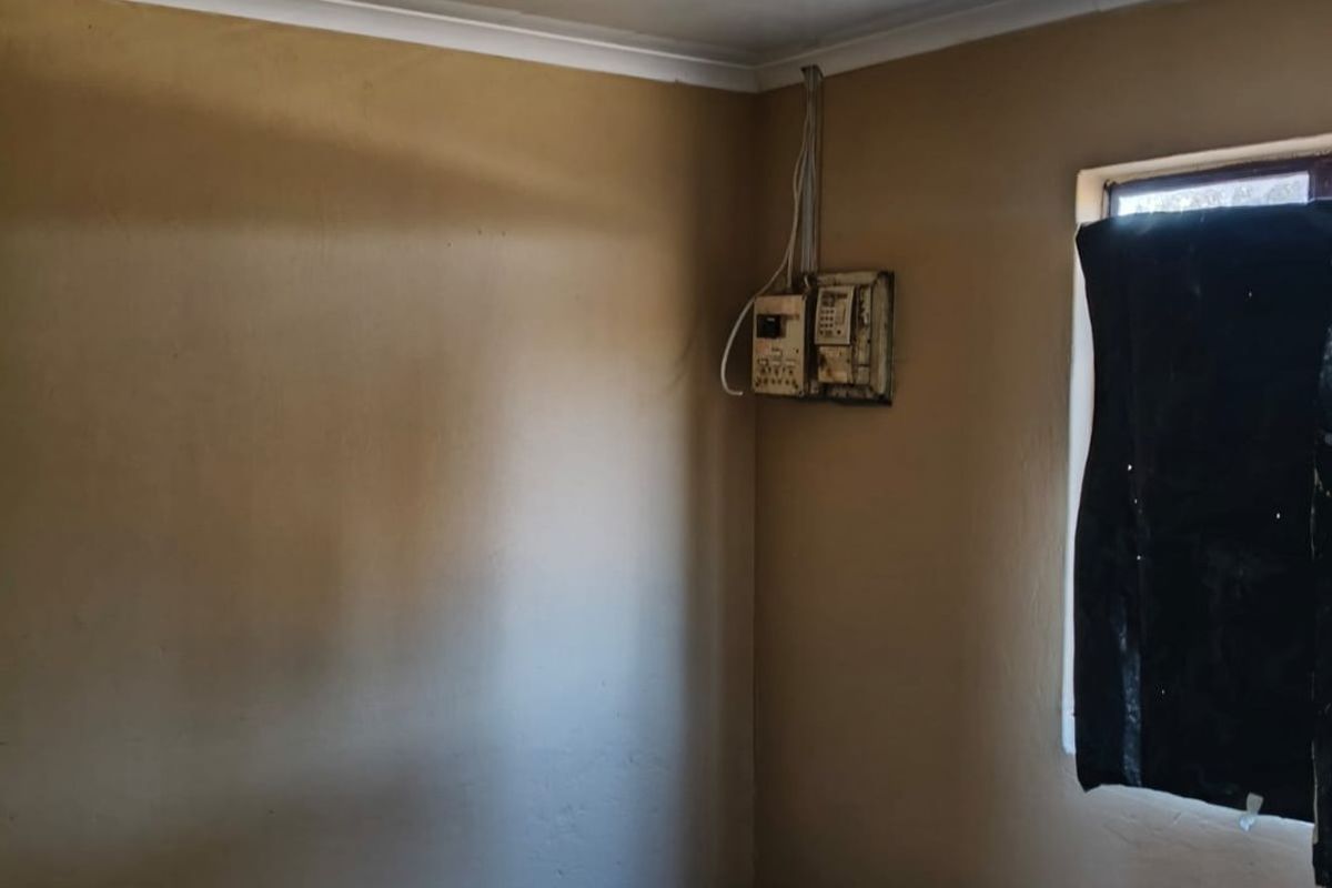 A bedroom featuring tiled flooring, a ceiling light fixture, and an exposed electrical distribution board on the wall.