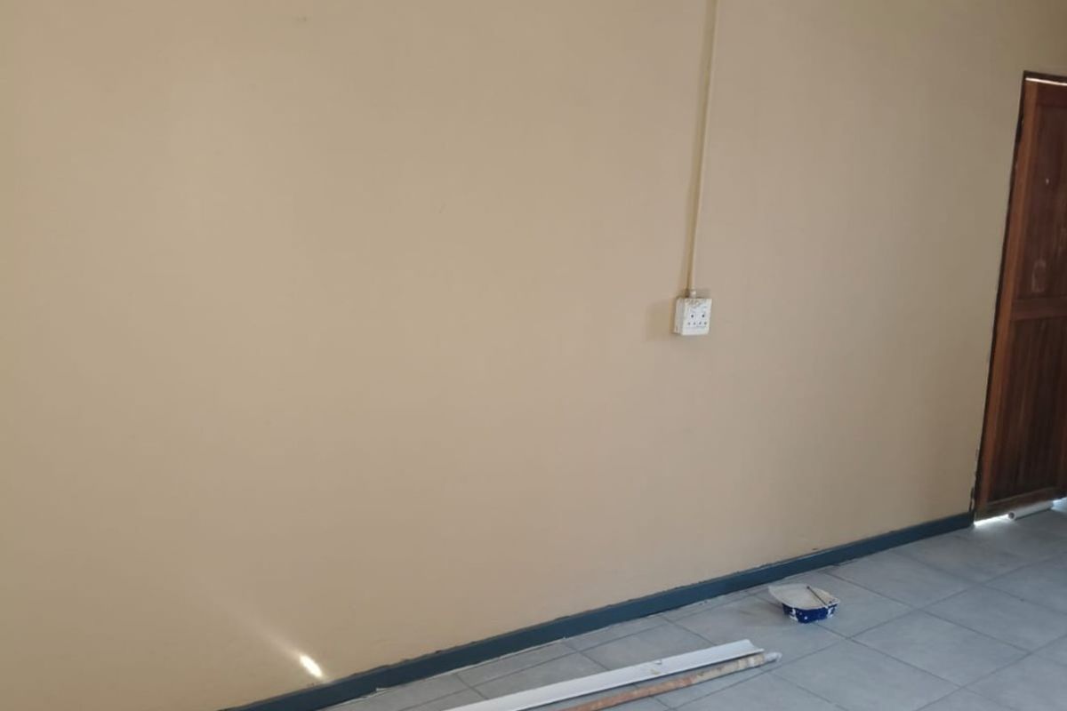 An empty living area featuring tiled flooring, cove cornicing, and a wooden door, currently undergoing minor maintenance or finishing work.