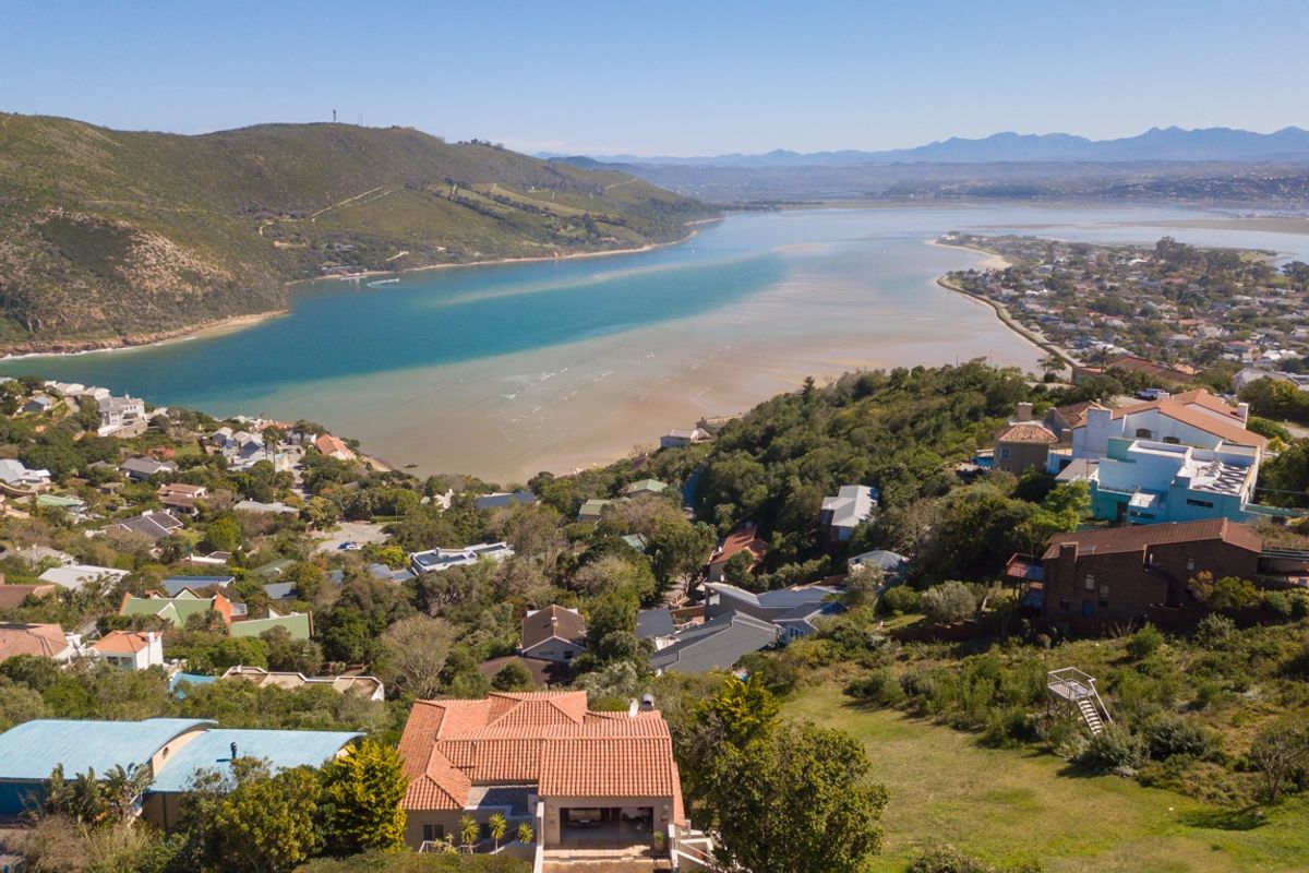 Aerial view of a residential property featuring a terracotta-tiled roof, overlooking a scenic coastal lagoon and surrounding hillside neighborhood.