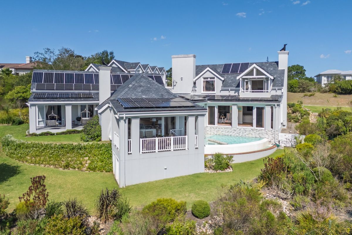 Aerial view of the rear elevation featuring a swimming pool, extensive solar panel installation, multiple balconies, and well-maintained landscaped gardens.