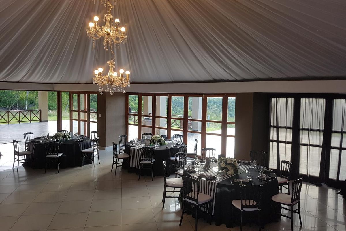 Spacious event hall featuring a draped ceiling, elegant crystal chandeliers, polished tile flooring, and expansive glass doors offering scenic views.