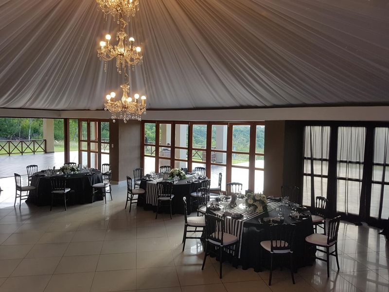 Spacious event hall featuring a draped ceiling, elegant crystal chandeliers, polished tile flooring, and expansive glass doors offering scenic views.