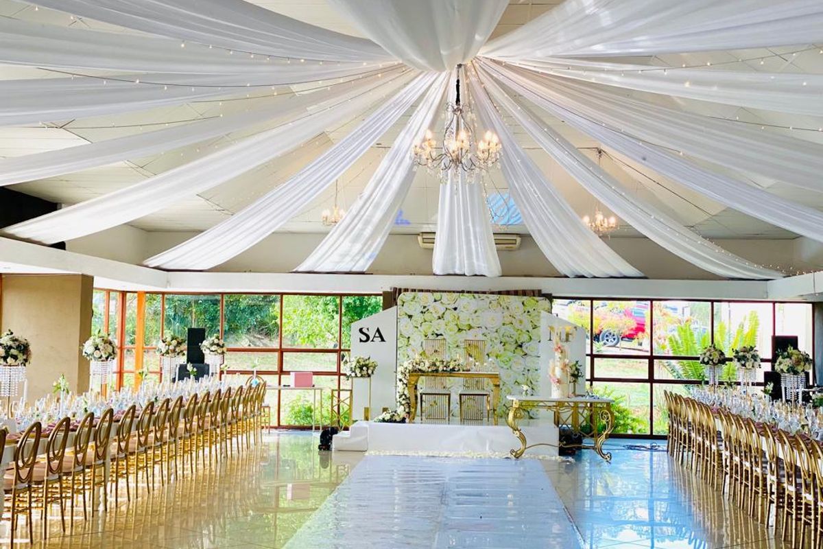 Spacious event hall featuring large format tiled flooring, extensive floor-to-ceiling windows, and decorative ceiling fabric draping, suitable for large gatherings or functions.