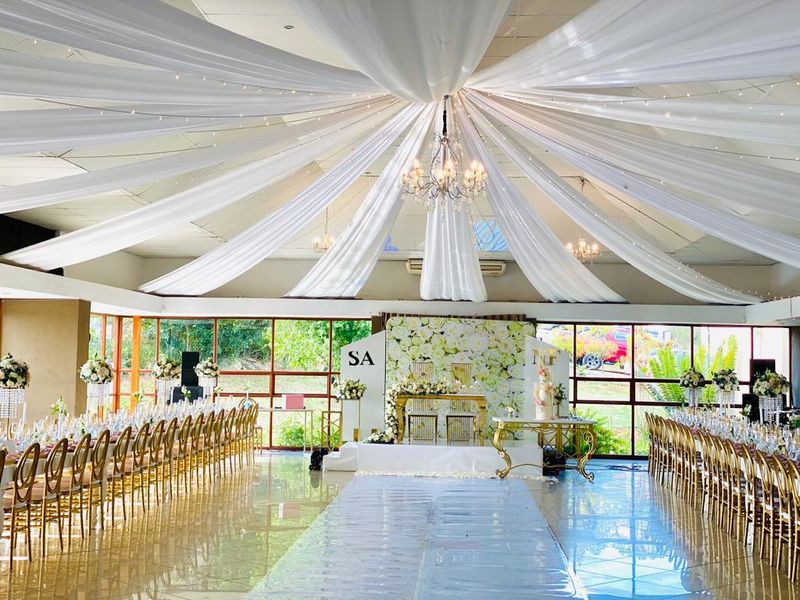 Spacious event hall featuring large format tiled flooring, extensive floor-to-ceiling windows, and decorative ceiling fabric draping, suitable for large gatherings or functions.