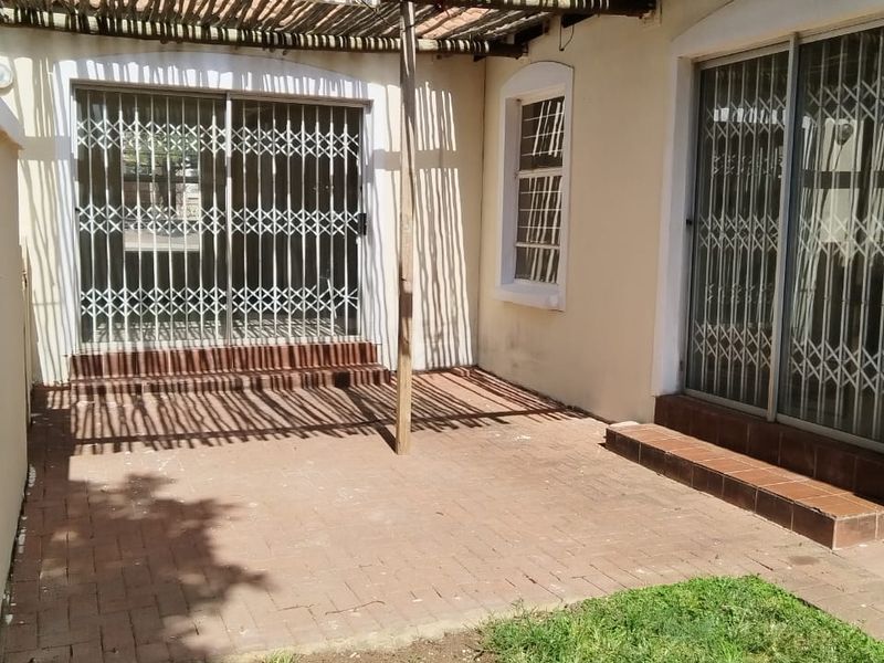 Outdoor patio area featuring brick paving, a rustic wooden pergola, and sliding glass doors with security gates providing access to the home.