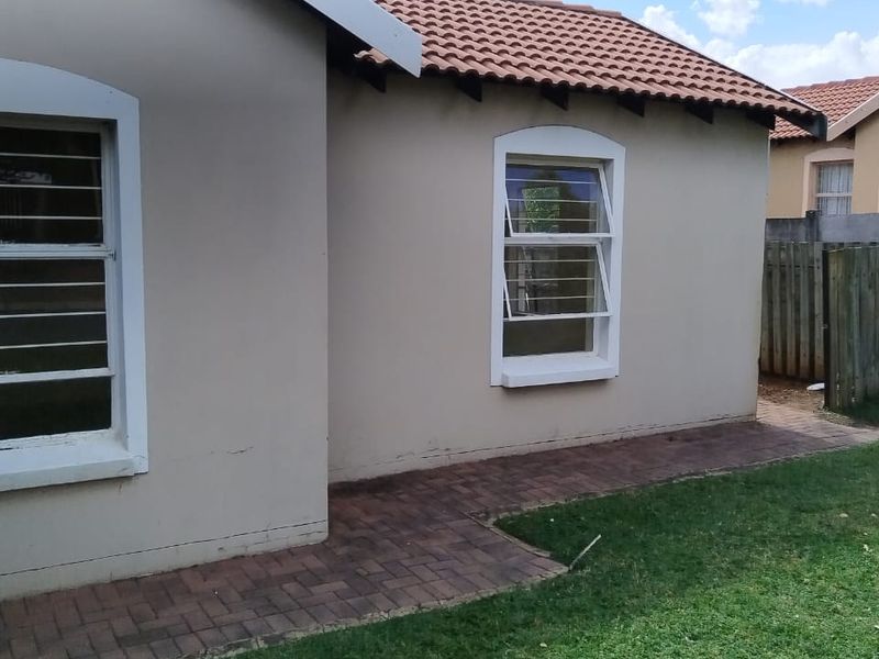A view of the rear exterior of the house featuring a tiled roof, paved walkway, and security-fitted windows.