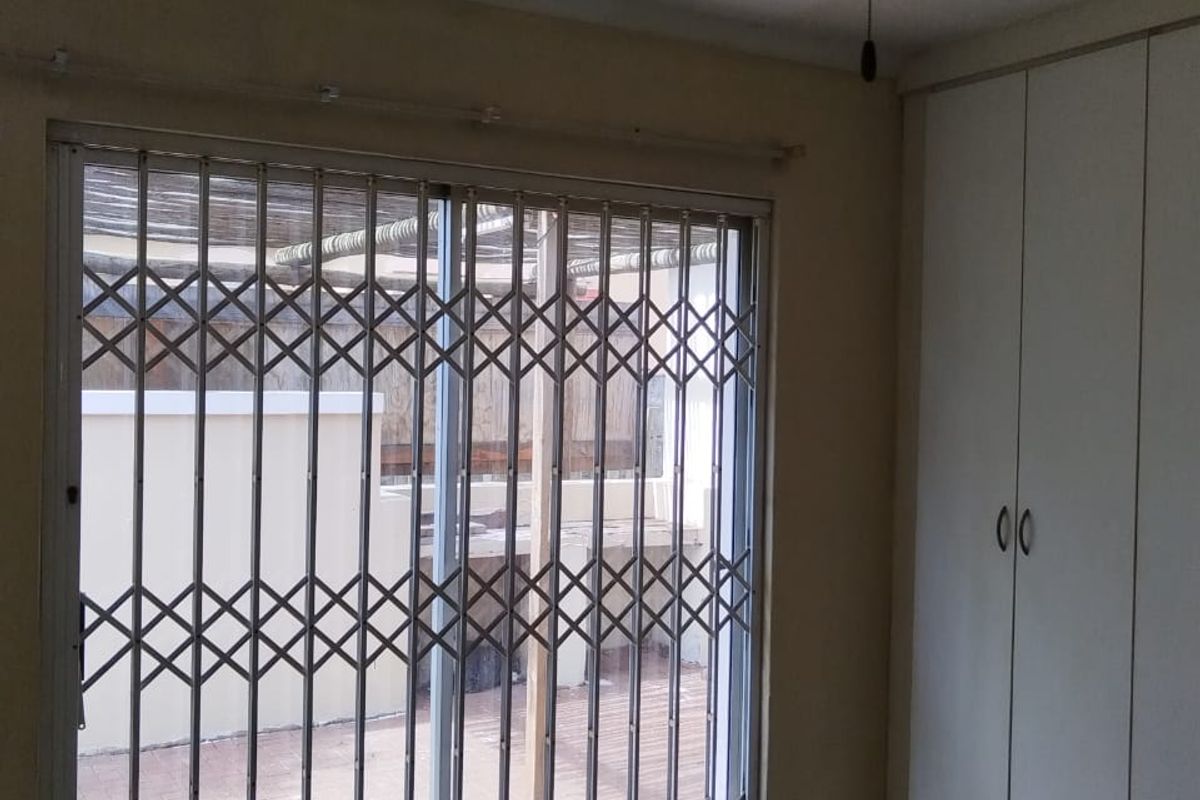 A bedroom featuring built-in cupboards, a ceiling fan, and a sliding glass door with a security gate leading to an outdoor area.