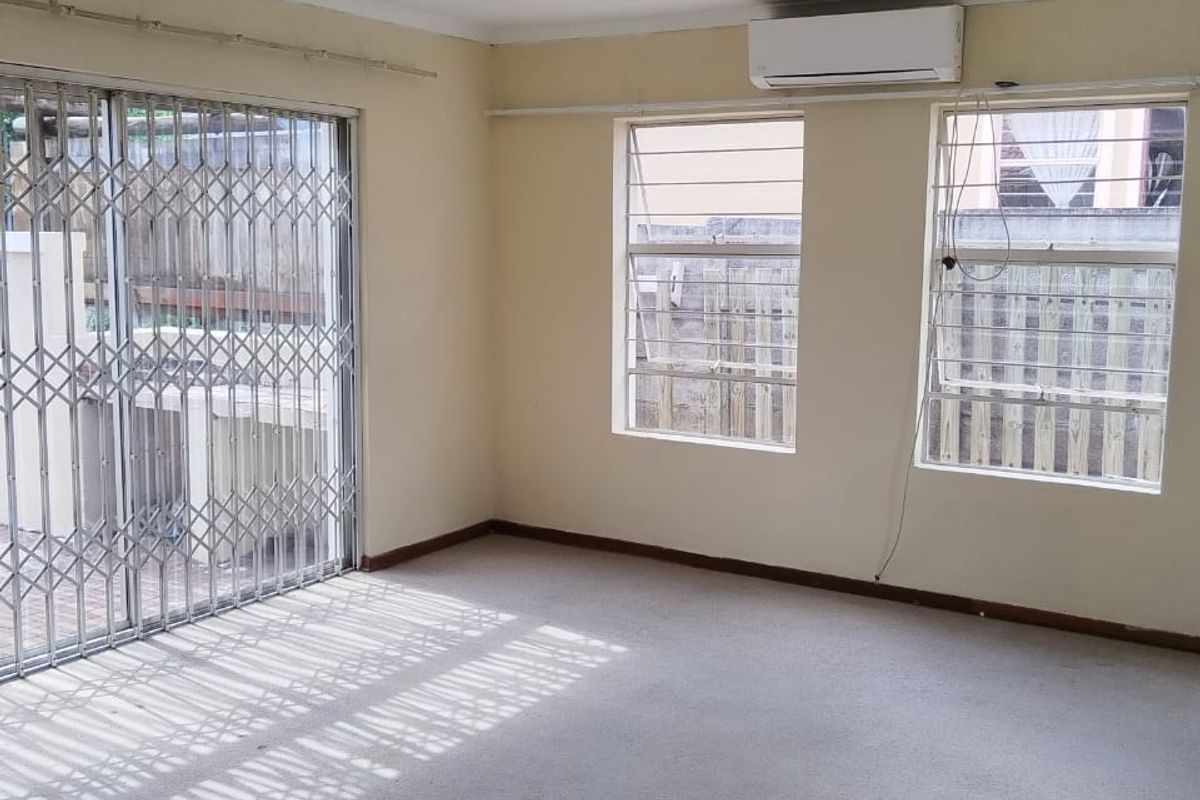 An empty living room featuring carpet flooring, a split-system air conditioner, and security gates leading to an outdoor area.