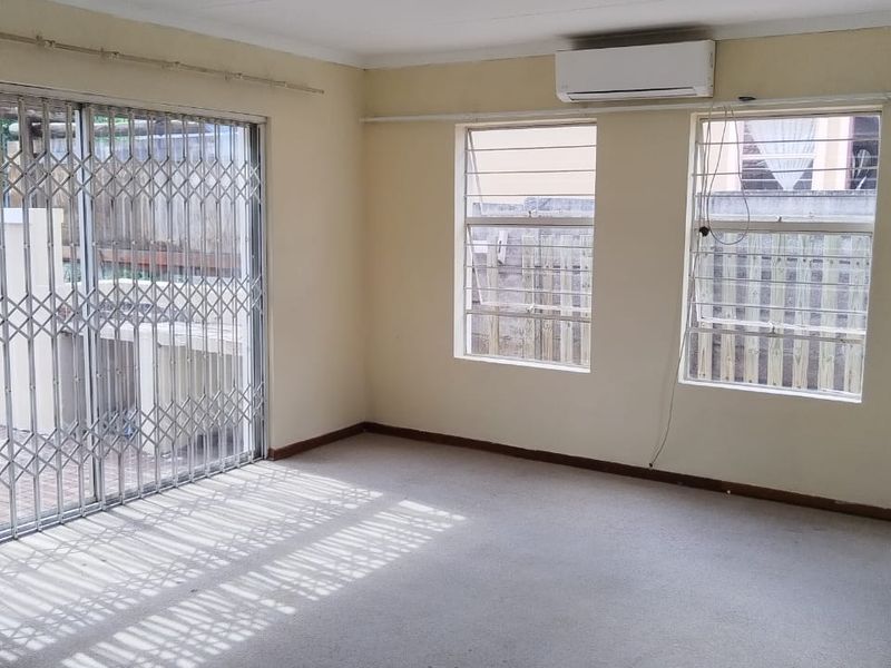 An empty living room featuring carpet flooring, a split-system air conditioner, and security gates leading to an outdoor area.