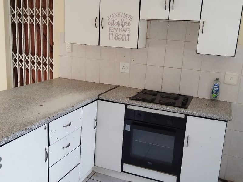 A functional kitchen featuring white cabinetry, a built-in oven and hob, tiled backsplash, and tiled flooring, with a security gate at the entrance.