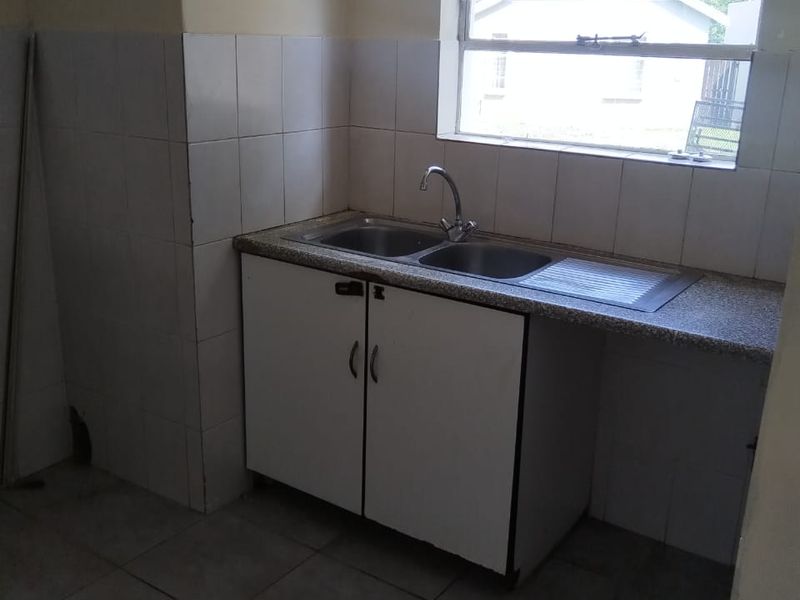 A functional kitchen area featuring a double bowl sink, tiled splashback, and base cabinetry, currently in need of cosmetic updates.