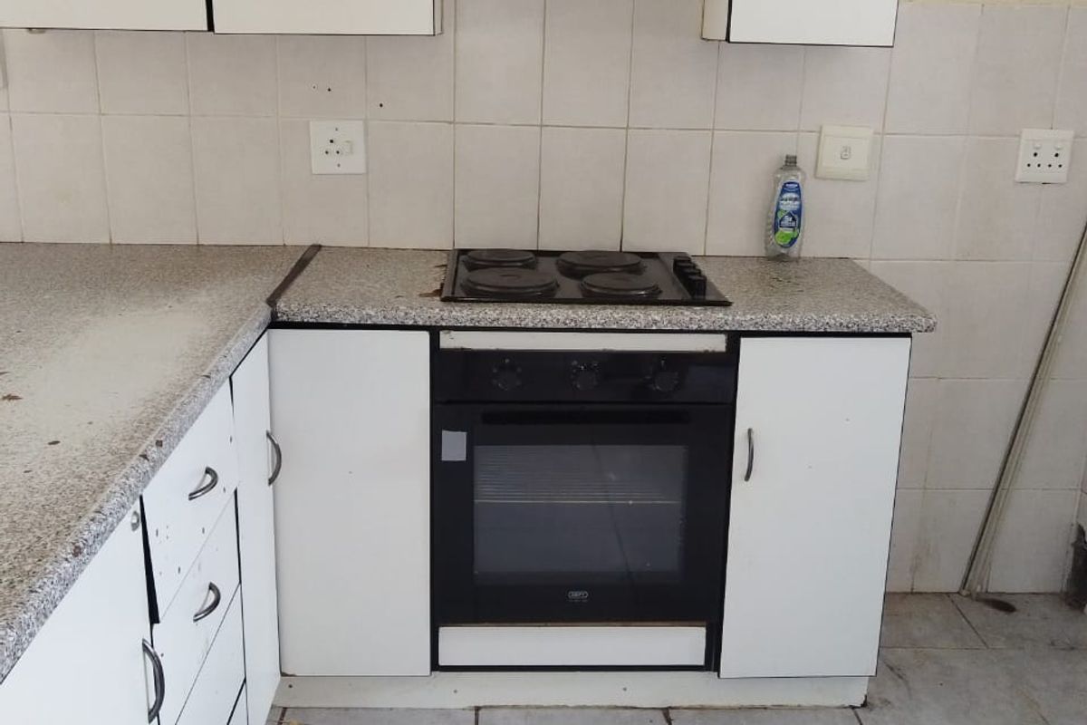 A dated kitchen featuring white cabinetry, a laminate countertop, and a built-in electric oven and hob, requiring cosmetic updates to improve its condition.