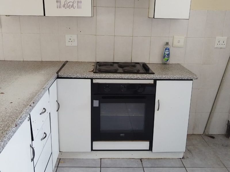 A dated kitchen featuring white cabinetry, a laminate countertop, and a built-in electric oven and hob, requiring cosmetic updates to improve its condition.