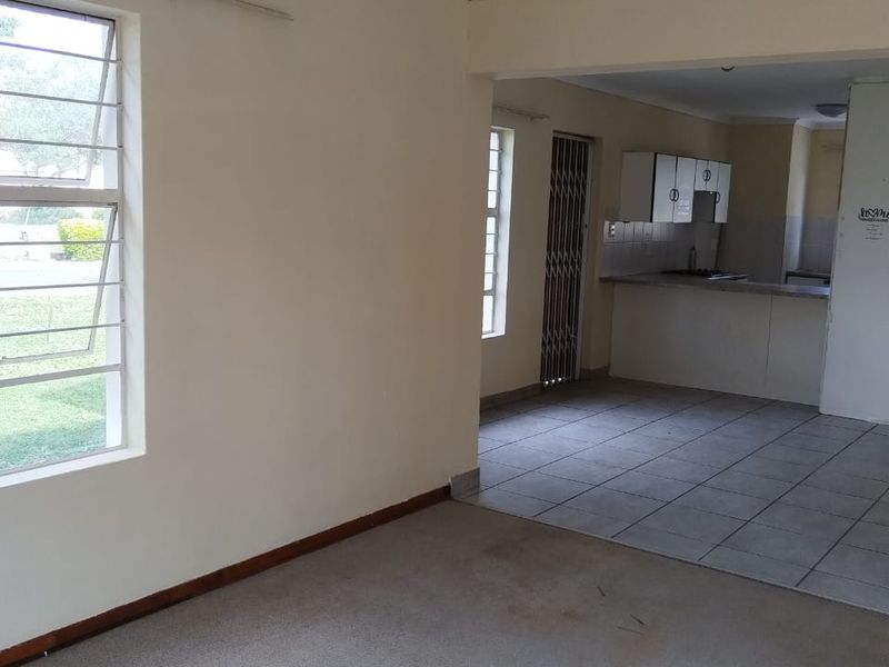 An open-plan living and kitchen area featuring carpeted flooring in the lounge, tiled kitchen floors, and built-in cabinetry.