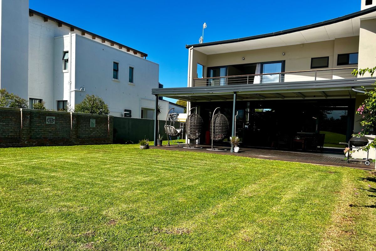 Rear view of the property featuring a spacious lawn, a covered timber deck patio, and an upper-level balcony.