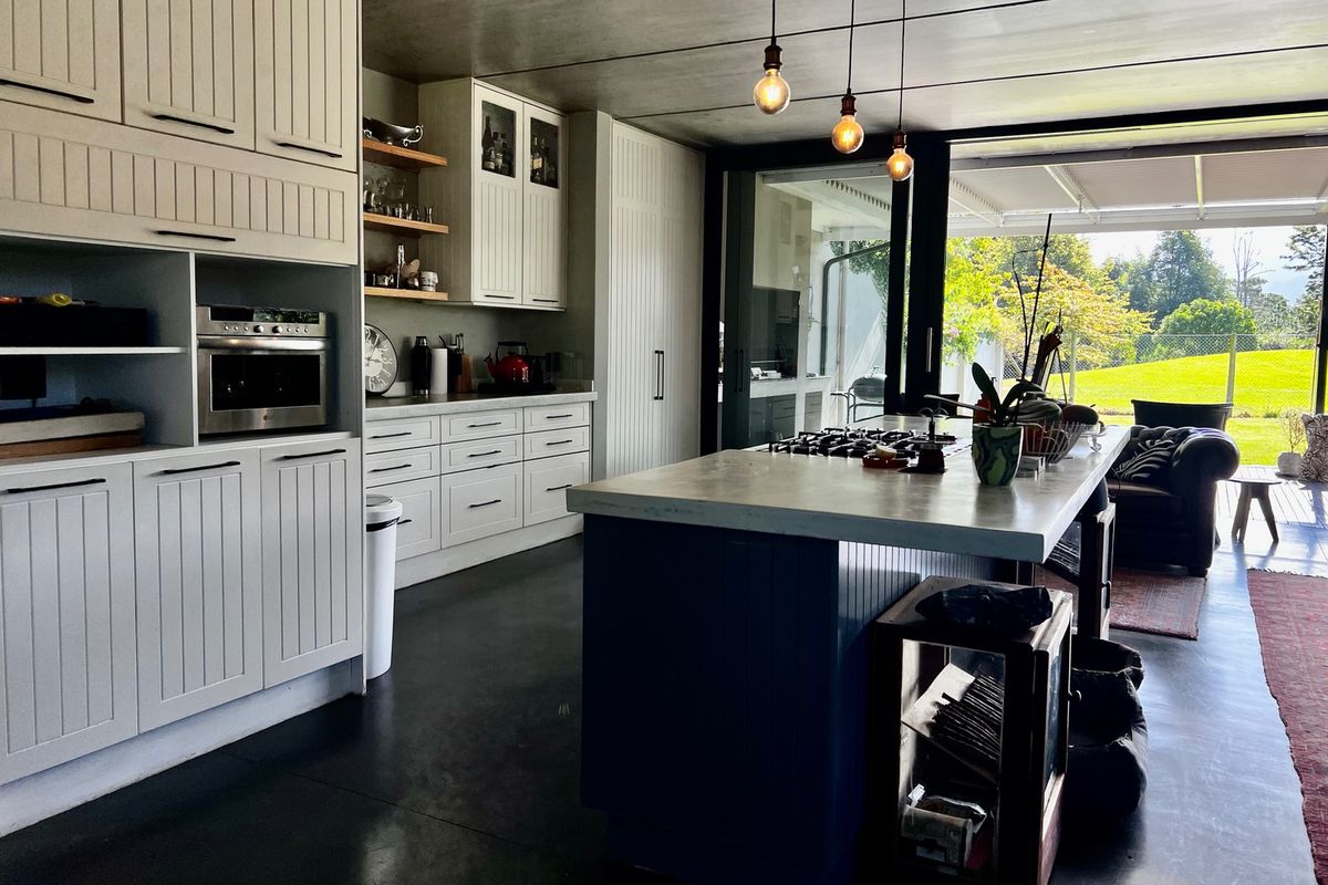 Modern kitchen featuring custom cabinetry, a central island with a gas hob, concrete ceiling, and seamless flow to an outdoor patio area.