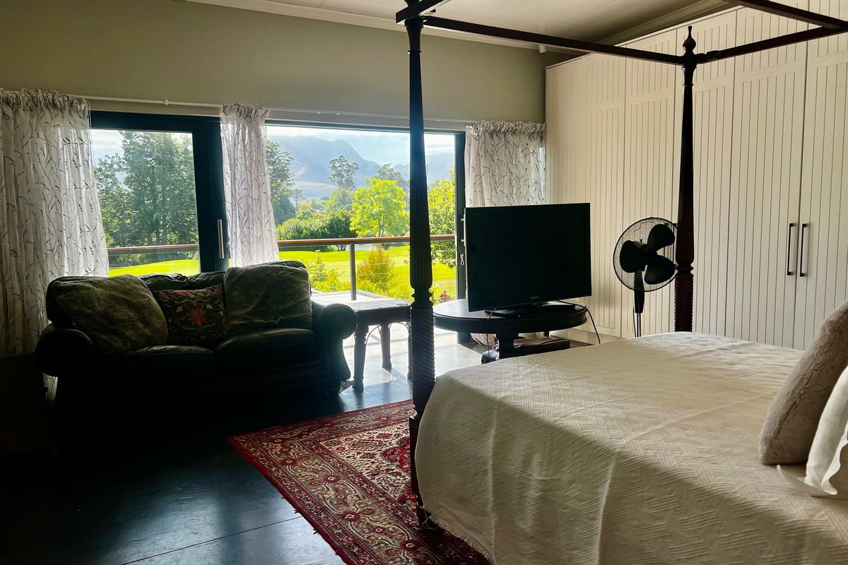 Spacious bedroom featuring built-in cupboards, dark tiled flooring, and large sliding doors opening onto a balcony with scenic garden and mountain views.