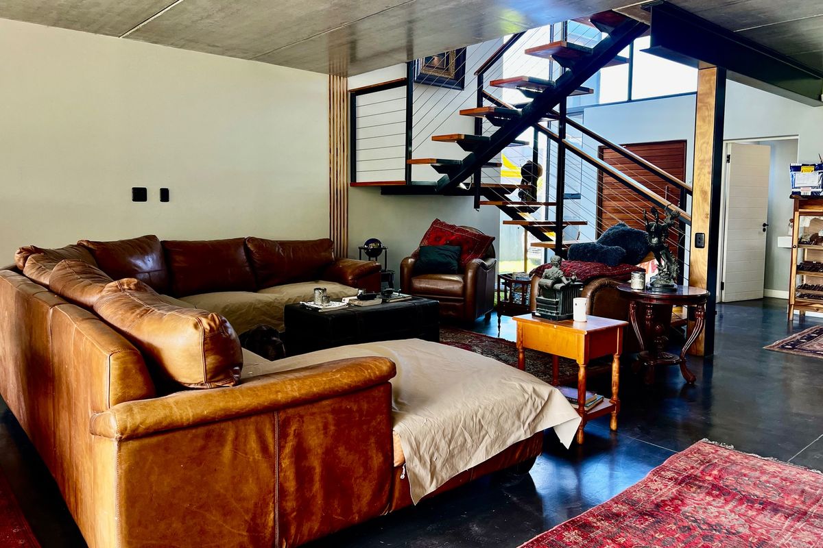 Spacious living area featuring an industrial aesthetic with an exposed concrete ceiling, polished concrete floors, and a striking floating staircase.