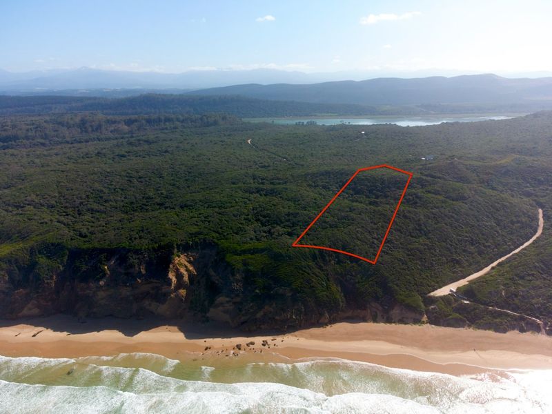 An aerial view of a vacant residential plot situated along the coastline, featuring natural vegetation and proximity to the beach.