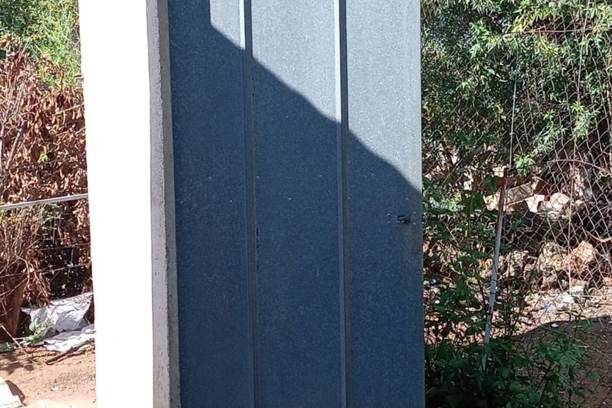 A standalone outdoor utility structure featuring a corrugated metal door and concrete base, situated in a garden setting.