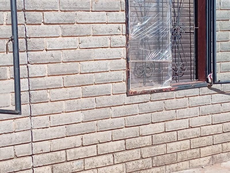 Exterior view of a brick wall showing a vertical structural crack and a window with a damaged security gate and plastic covering.