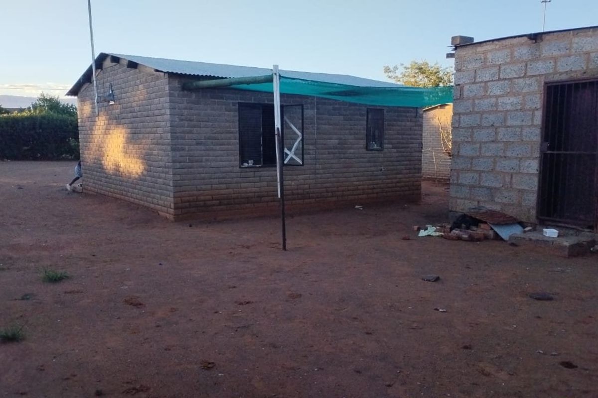 Rear view of a basic concrete block structure with a corrugated metal roof and a simple shade cloth awning area.