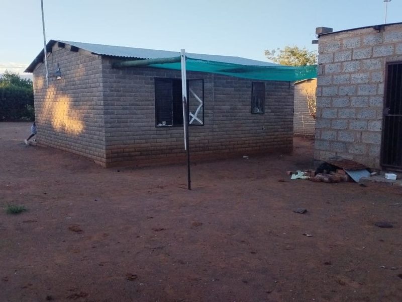 Rear view of a basic concrete block structure with a corrugated metal roof and a simple shade cloth awning area.