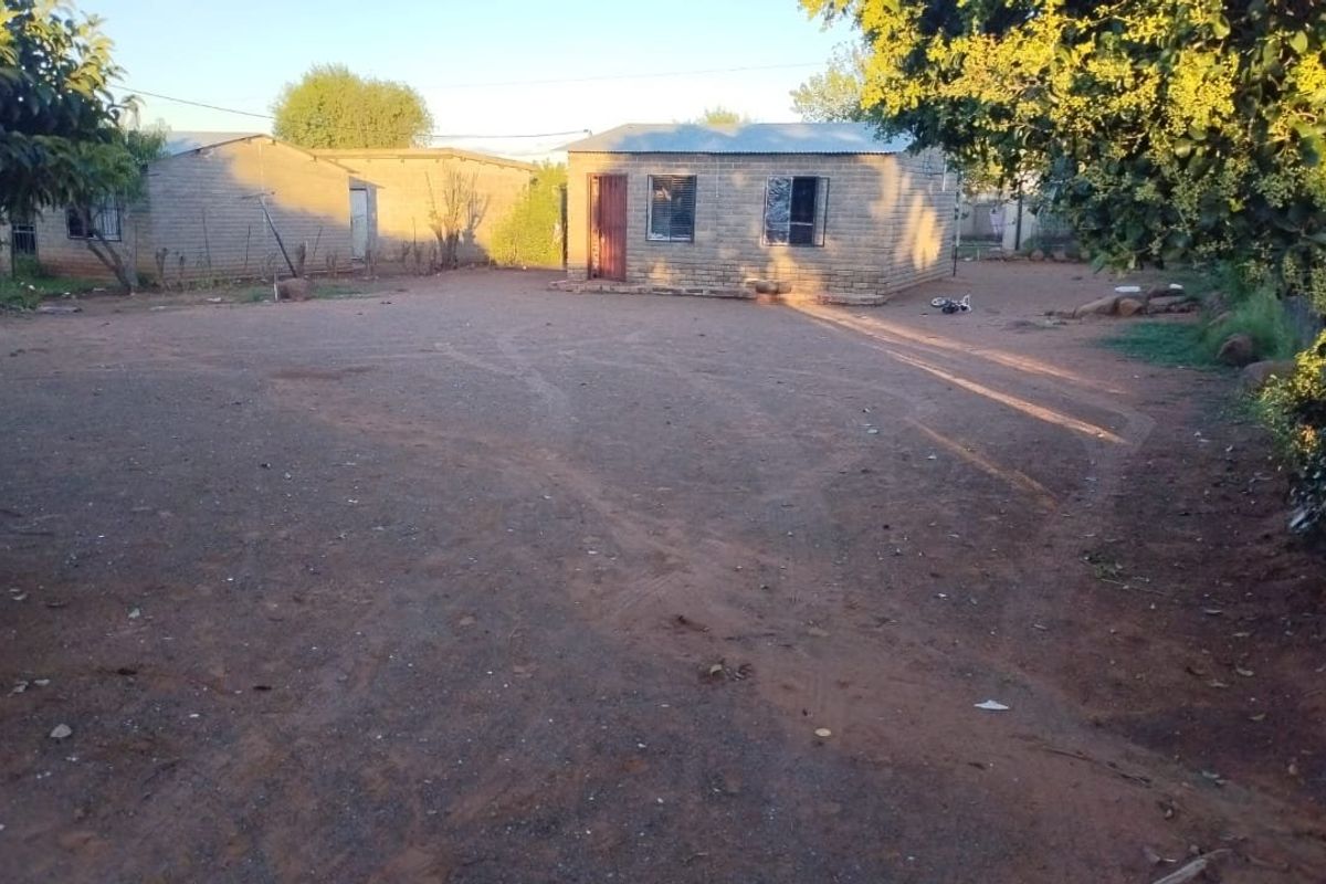 A view of the rear yard featuring exposed brick structures with corrugated metal roofing and metal window frames set in an unpaved outdoor area.