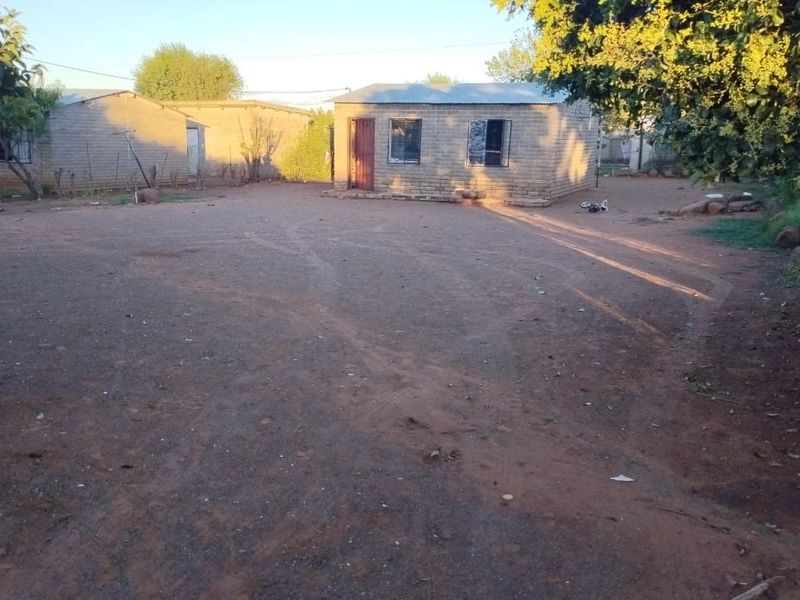 A view of the rear yard featuring exposed brick structures with corrugated metal roofing and metal window frames set in an unpaved outdoor area.