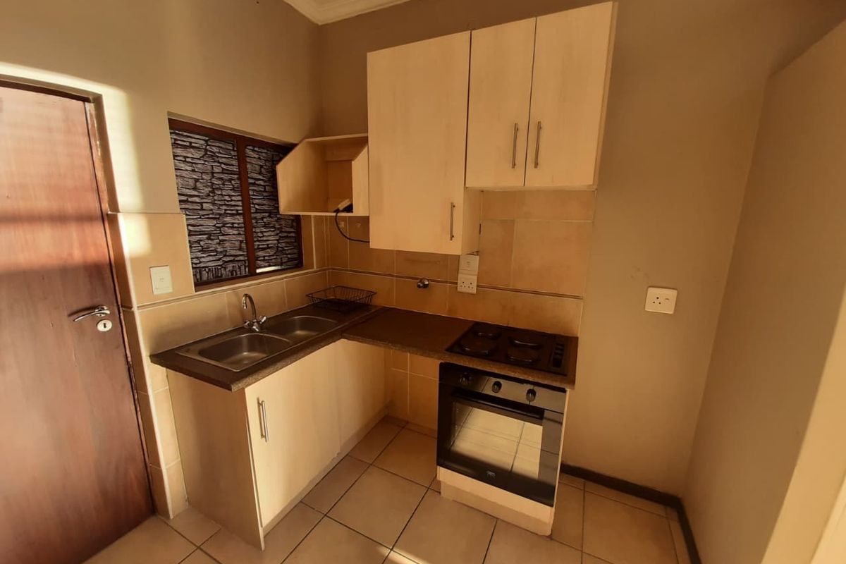 A compact kitchen featuring built-in cabinetry, a double sink, and an integrated oven with an electric hob, finished with tiled flooring and backsplash.