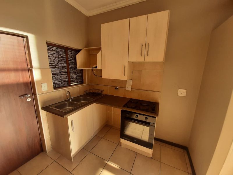 A compact kitchen featuring built-in cabinetry, a double sink, and an integrated oven with an electric hob, finished with tiled flooring and backsplash.
