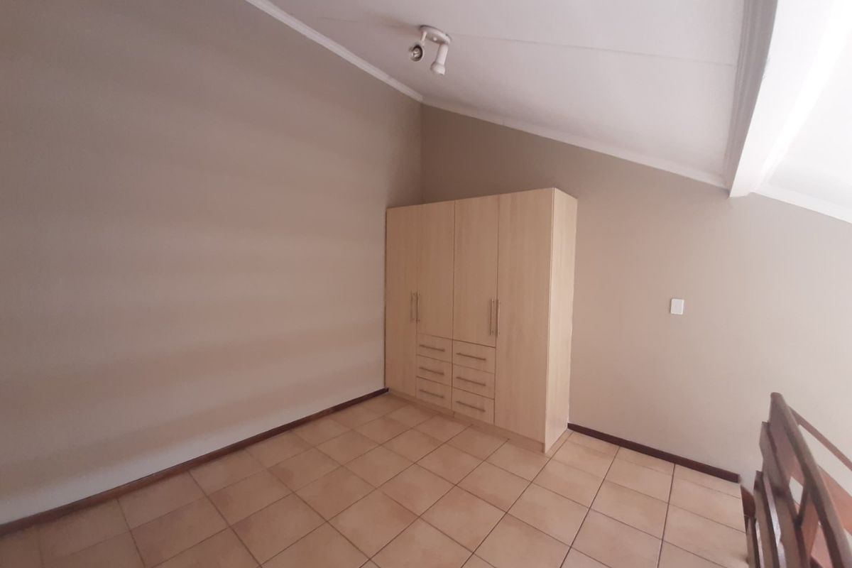 A spacious bedroom featuring neutral walls, tiled flooring, a sloped ceiling, and a functional built-in wardrobe.