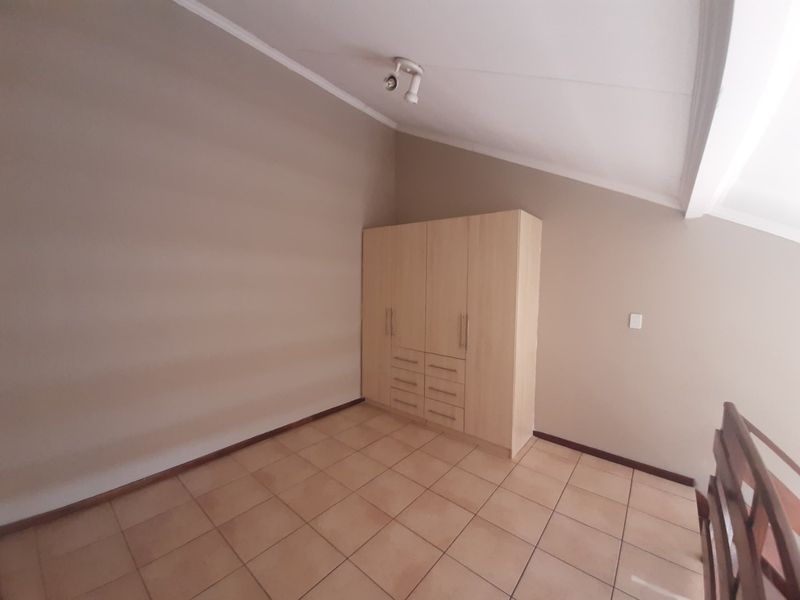 A spacious bedroom featuring neutral walls, tiled flooring, a sloped ceiling, and a functional built-in wardrobe.